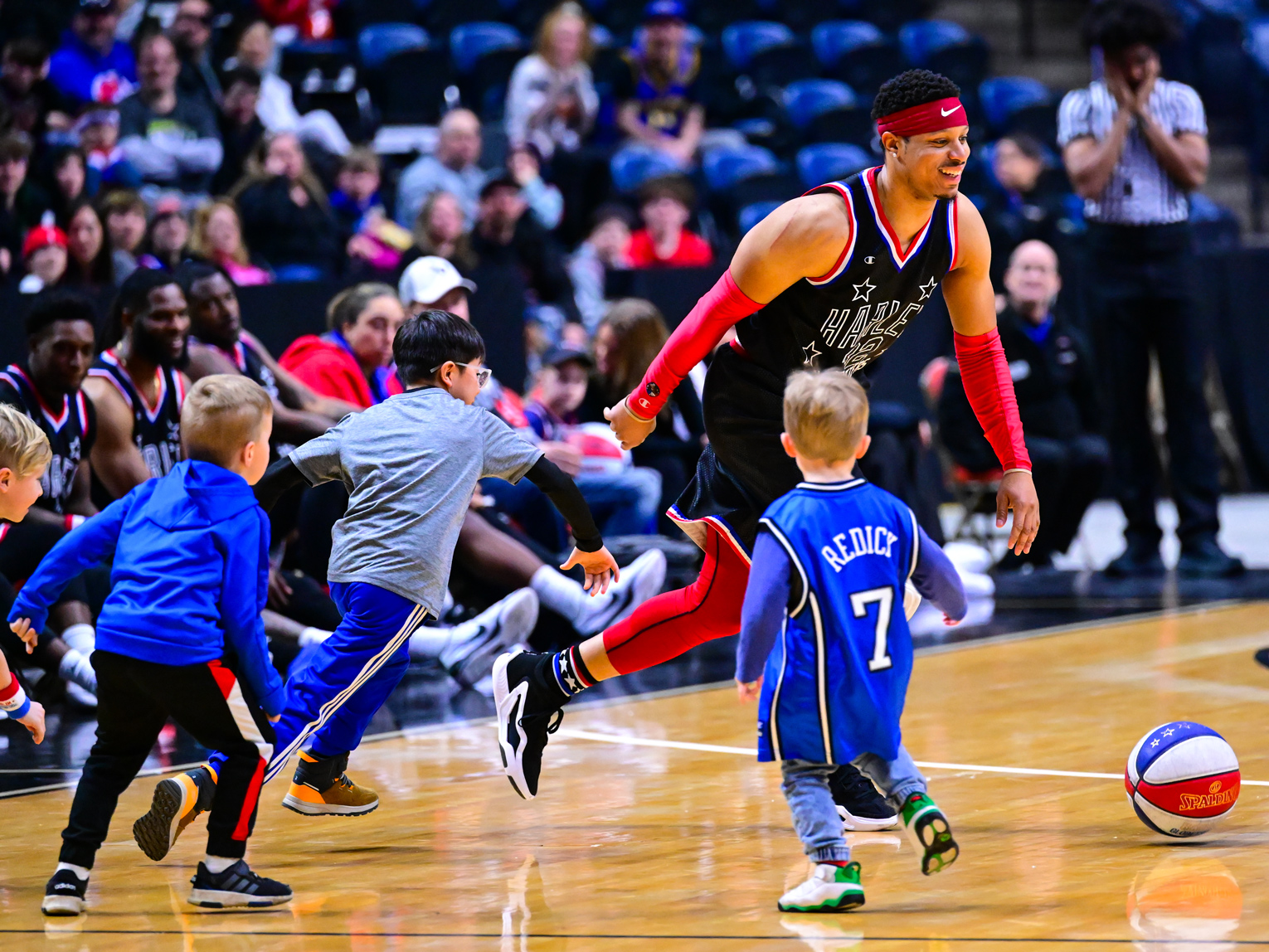 Ein Spieler der Harlem Globetrotters spielt gegen vier kleine Jungs Basketball.