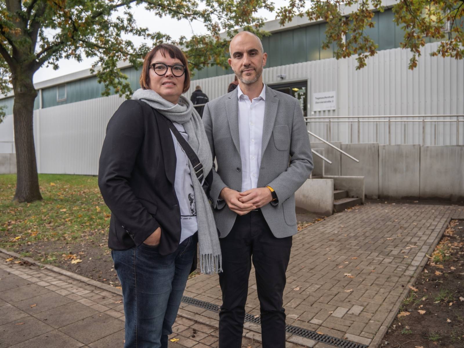 Eine Frau und ein Mann stehen vor einer Halle.