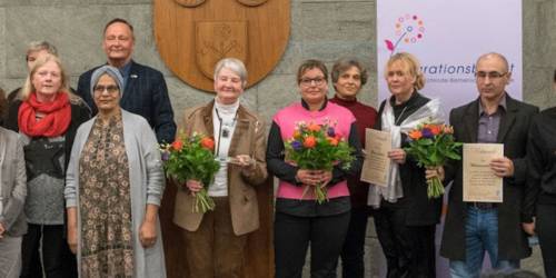 Gruppenfoto Integrationsbeirat. Siebzehn Menschen stehen für ein Foto zusammen vor einem Roll-Up mit der Aufschrift Integrationsbeirat.