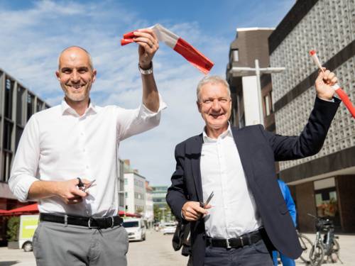 Zwei Männer auf einer Straße, die ein Band durchschneiden.