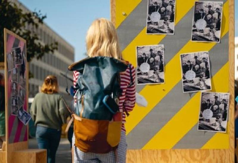 Frau mit Rucksack vor einer Fotowand im Freien. Das Historische Museum Hannover beim Innenstadtdialog "Hannover Mit(te) gestalten", 2. Experimentierraum, 2021, Fotograf Ulrich Pucknat