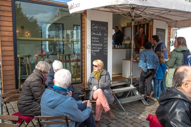 Menschen sitzen in einem Straßencafé auf dem Wochenmarkt.