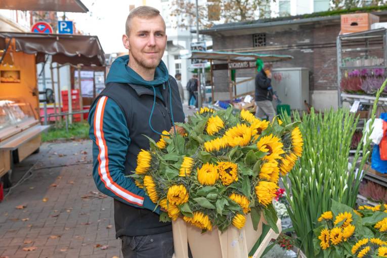 Ein Mann hält eine Kiste voll gelber Blumen in die Kamera.